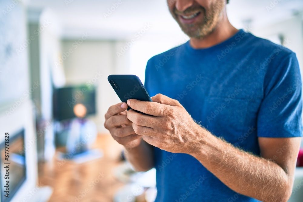 Young irish man smiling happy using smartphone standing at home. Young irish man smiling happy using smartphone standing at home.
