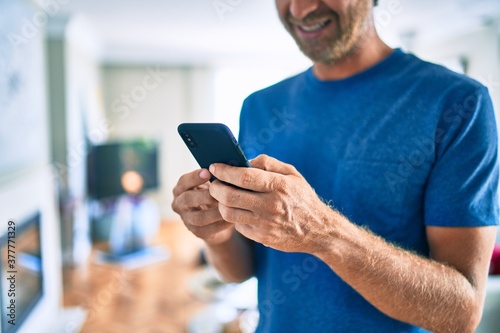 Young irish man smiling happy using smartphone standing at home.