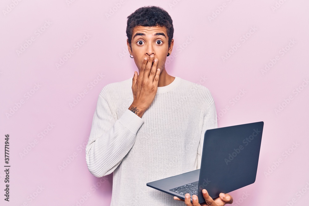 Young african amercian man holding laptop covering mouth with hand, shocked and afraid for mistake. surprised expression Young african amercian man holding laptop covering mouth with hand, shocked and afraid for mistake. surprised expression