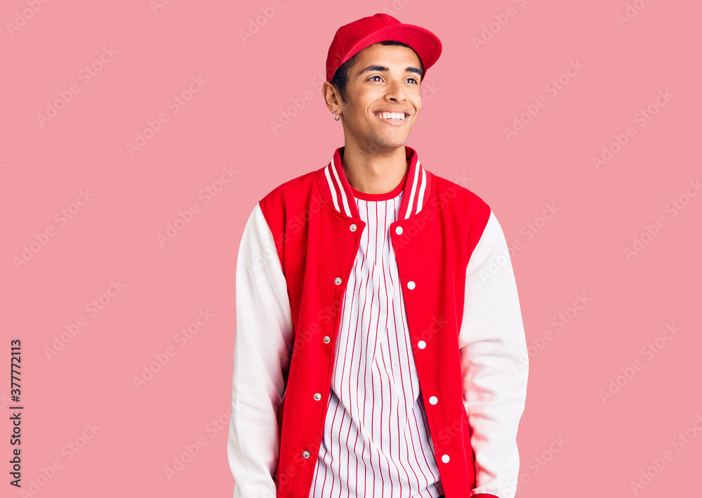 Young african amercian man wearing baseball uniform looking away to side with smile on face, natural expression. laughing confident. Young african amercian man wearing baseball uniform looking away to side with smile on face, natural expression. laughing confident.