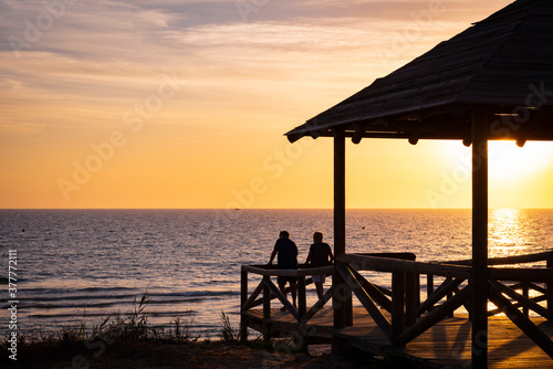 Fototapeta Naklejka Na Ścianę i Meble -  Pareja mirando el atardecer en la playa de Costa Ballena, ubicada entre Rota y Chipiona, provincia de Cádiz, España, 9 de septiembre de 2020