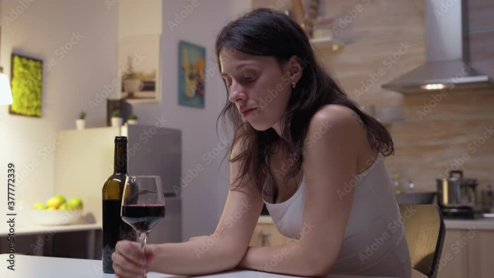 Alcohol addiction wife drinking in the kitchen. Unhappy person suffering of migraine, depression, disease and anxiety feeling exhausted with dizziness symptoms having alcoholism problems. Alcohol addiction wife drinking in the kitchen. Unhappy person suffering of migraine, depression, disease and anxiety feeling exhausted with dizziness symptoms having alcoholism problems.