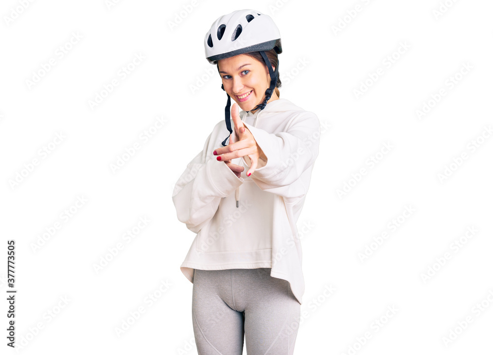 Beautiful brunette young woman wearing bike helmet and sporty clothes pointing fingers to camera with happy and funny face. good energy and vibes. Beautiful brunette young woman wearing bike helmet and sporty clothes pointing fingers to camera with happy and funny face. good energy and vibes.