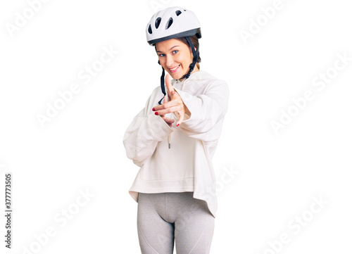 Beautiful brunette young woman wearing bike helmet and sporty clothes pointing fingers to camera with happy and funny face. good energy and vibes.