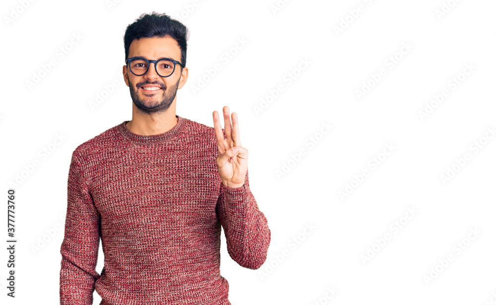 Young handsome hispanic man wearing winter sweater and glasses showing and pointing up with fingers number three while smiling confident and happy. Young handsome hispanic man wearing winter sweater and glasses showing and pointing up with fingers number three while smiling confident and happy.