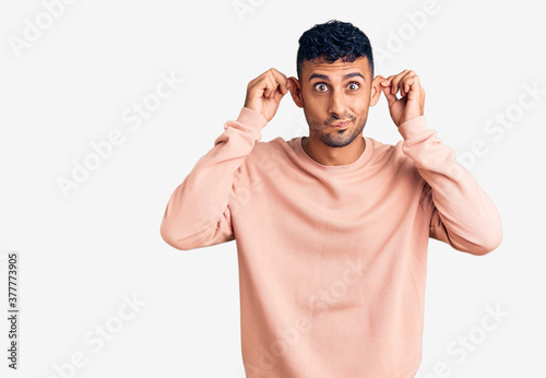 Young hispanic man wearing casual clothes smiling pulling ears with fingers, funny gesture. audition problem