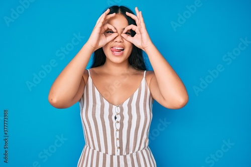 Young beautiful asian girl wearing casual clothes doing ok gesture like binoculars sticking tongue out, eyes looking through fingers. crazy expression.