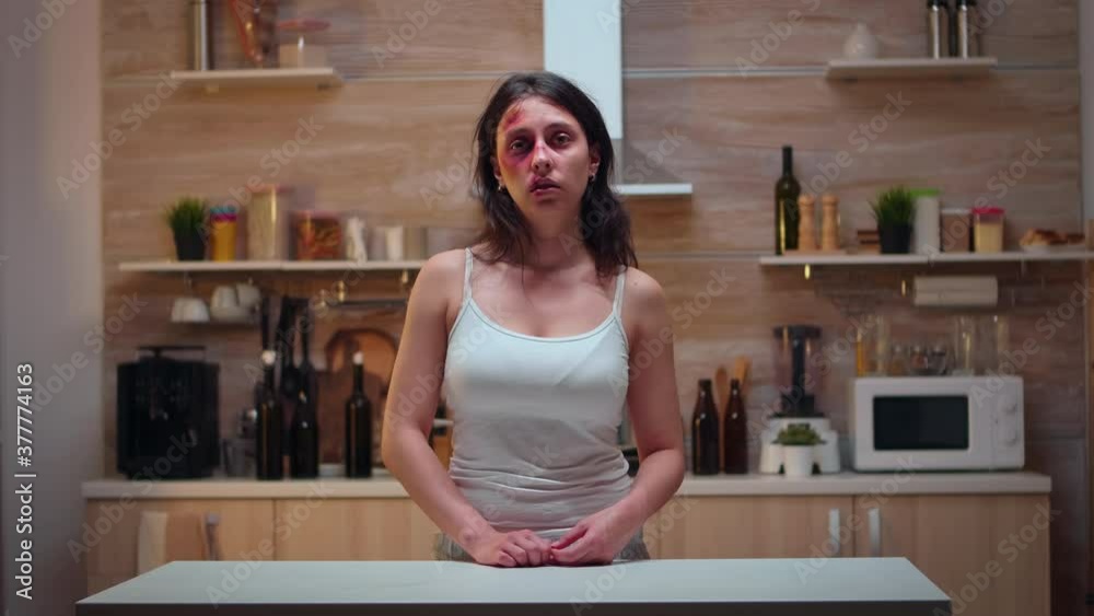 Traumatised woman sitting in the kitchen looking at the camera. Violent aggressive man abusing injuring terrified helpless, vulnerable, afraid, beaten and panicked wife living in terror and pressure Traumatised woman sitting in the kitchen looking at the camera. Violent aggressive man abusing injuring terrified helpless, vulnerable, afraid, beaten and panicked wife living in terror and pressure