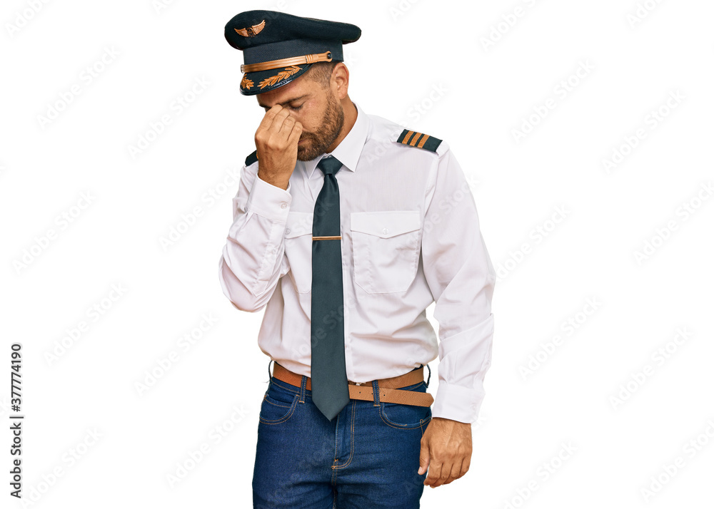 Handsome man with beard wearing airplane pilot uniform tired rubbing nose and eyes feeling fatigue and headache. stress and frustration concept.
