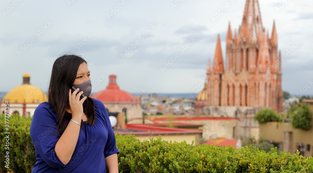 
Selfie with mobile phone of Latina tourist woman with protection mask on terrace with cathedral view in San Miguel de Allende, Guanajuato Mexico