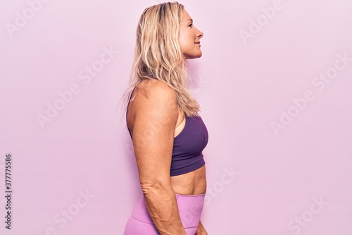 Middle age caucasian blonde woman wearing sportswear over pink background looking to side, relax profile pose with natural face with confident smile.