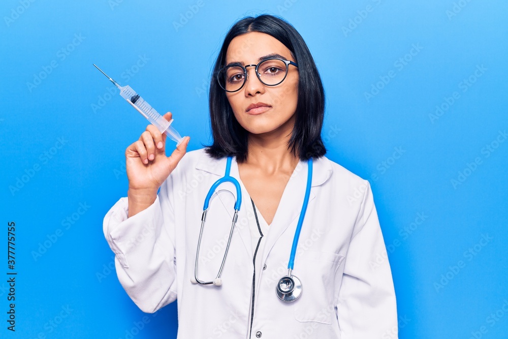Young beautiful latin woman wearing doctor stethoscope holding syringe thinking attitude and sober expression looking self confident Young beautiful latin woman wearing doctor stethoscope holding syringe thinking attitude and sober expression looking self confident