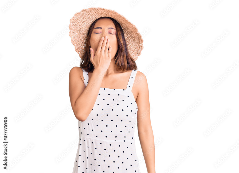 Young beautiful chinese girl wearing summer hat bored yawning tired covering mouth with hand. restless and sleepiness. Young beautiful chinese girl wearing summer hat bored yawning tired covering mouth with hand. restless and sleepiness.