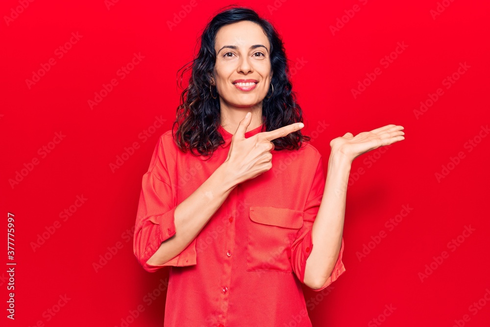Naklejka premium Young beautiful hispanic woman wearing casual clothes amazed and smiling to the camera while presenting with hand and pointing with finger.