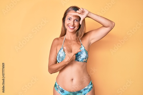 Middle age hispanic woman wearing bikini smiling making frame with hands and fingers with happy face. creativity and photography concept. photo