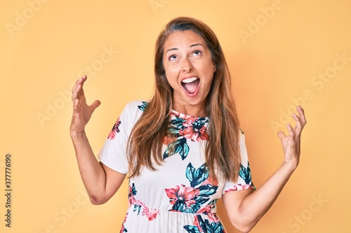 Middle age hispanic woman wearing casual floral dress crazy and mad shouting and yelling with aggressive expression and arms raised. frustration concept.