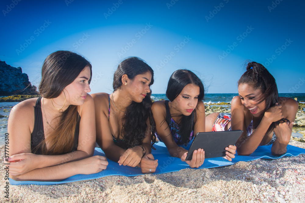 Group latin american girls friends using social media in digital tablet at beach in Summer time Group latin american girls friends using social media in digital tablet at beach in Summer time