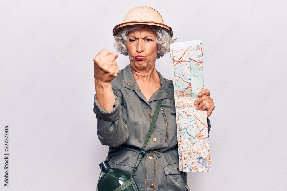 Senior grey-haired woman wearing explorer hat holding map annoyed and frustrated shouting with anger, yelling crazy with anger and hand raised