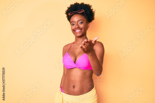 Young african american woman wearing bikini smiling friendly offering handshake as greeting and welcoming. successful business.