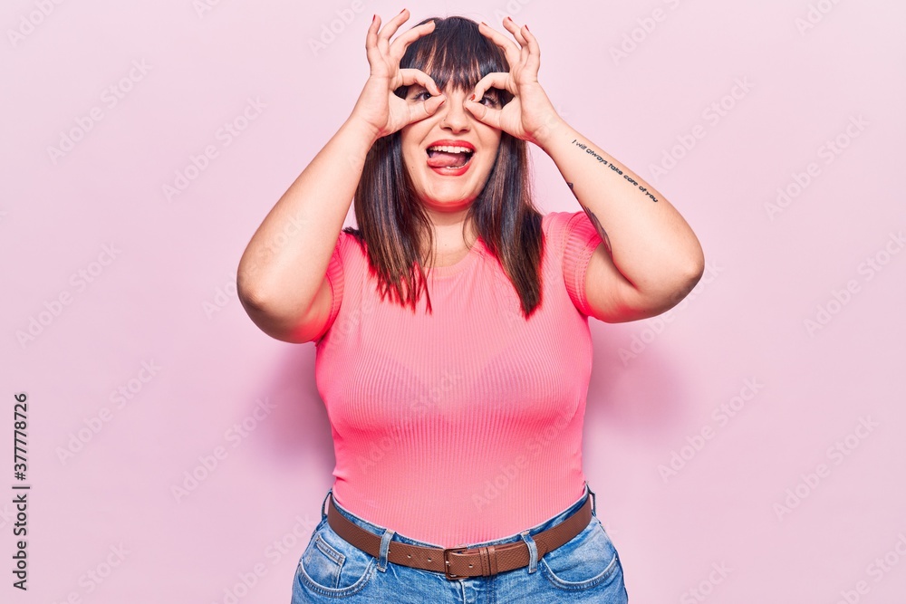 Young plus size woman wearing casual clothes doing ok gesture like binoculars sticking tongue out, eyes looking through fingers. crazy expression. Young plus size woman wearing casual clothes doing ok gesture like binoculars sticking tongue out, eyes looking through fingers. crazy expression.