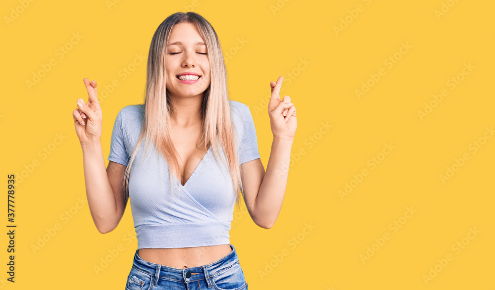 Young beautiful blonde woman wearing casual clothes gesturing finger crossed smiling with hope and eyes closed. luck and superstitious concept. Young beautiful blonde woman wearing casual clothes gesturing finger crossed smiling with hope and eyes closed. luck and superstitious concept.