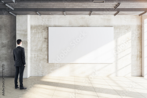 Businessman looking on blank poster on concrete wall.
