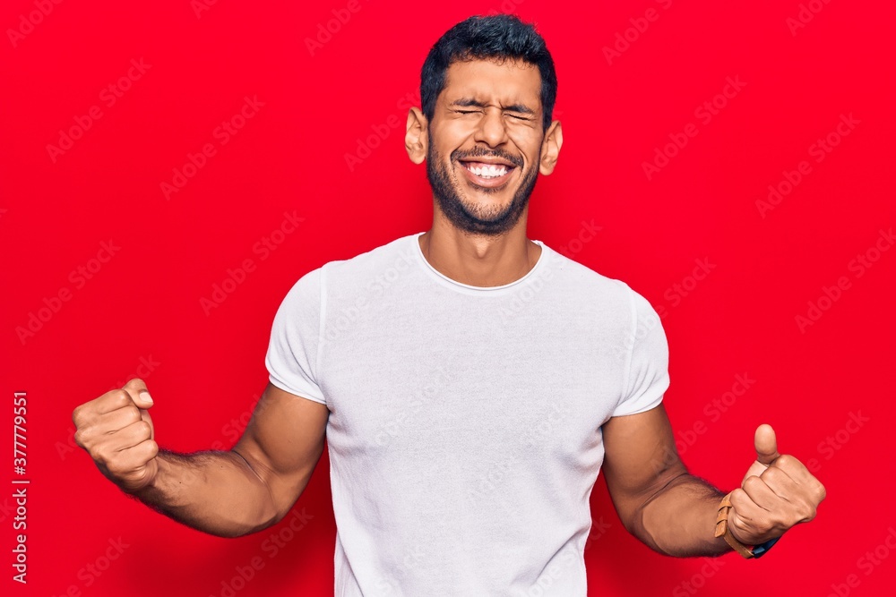 Young latin man wearing casual clothes very happy and excited doing winner gesture with arms raised, smiling and screaming for success. celebration concept. Young latin man wearing casual clothes very happy and excited doing winner gesture with arms raised, smiling and screaming for success. celebration concept.