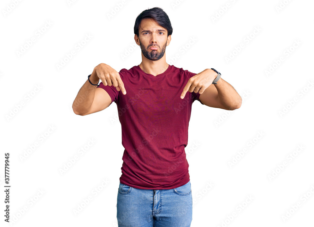 Naklejka premium Handsome hispanic man wearing casual clothes pointing down looking sad and upset, indicating direction with fingers, unhappy and depressed.