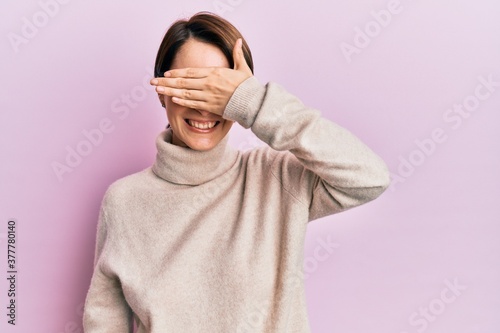 Young brunette woman with short hair wearing casual winter sweater smiling and laughing with hand on face covering eyes for surprise. blind concept. © Krakenimages.com