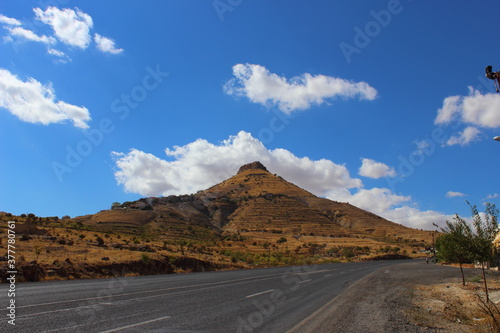 the road to the mountains under sharp clouds and blue sky, clouds are near to the ground