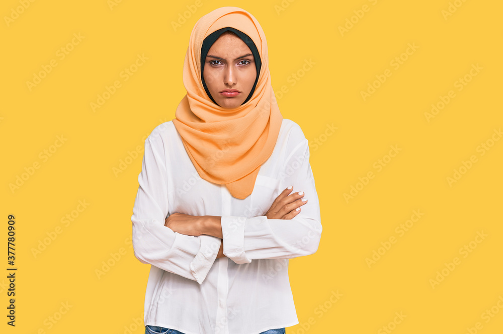 Young brunette woman wearing traditional islamic hijab scarf skeptic and nervous, disapproving expression on face with crossed arms. negative person.