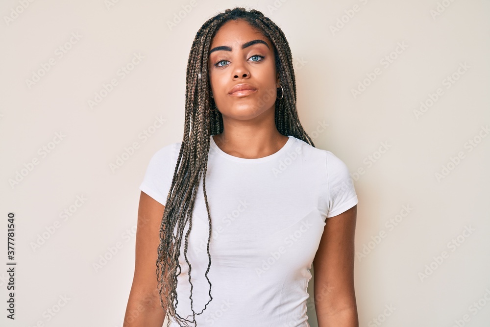 Young african american woman with braids wearing casual white tshirt relaxed with serious expression on face. simple and natural looking at the camera. Young african american woman with braids wearing casual white tshirt relaxed with serious expression on face. simple and natural looking at the camera.