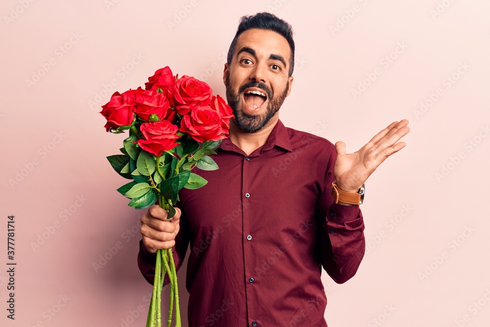 Young hispanic man holding flowers celebrating achievement with happy smile and winner expression with raised hand Young hispanic man holding flowers celebrating achievement with happy smile and winner expression with raised hand