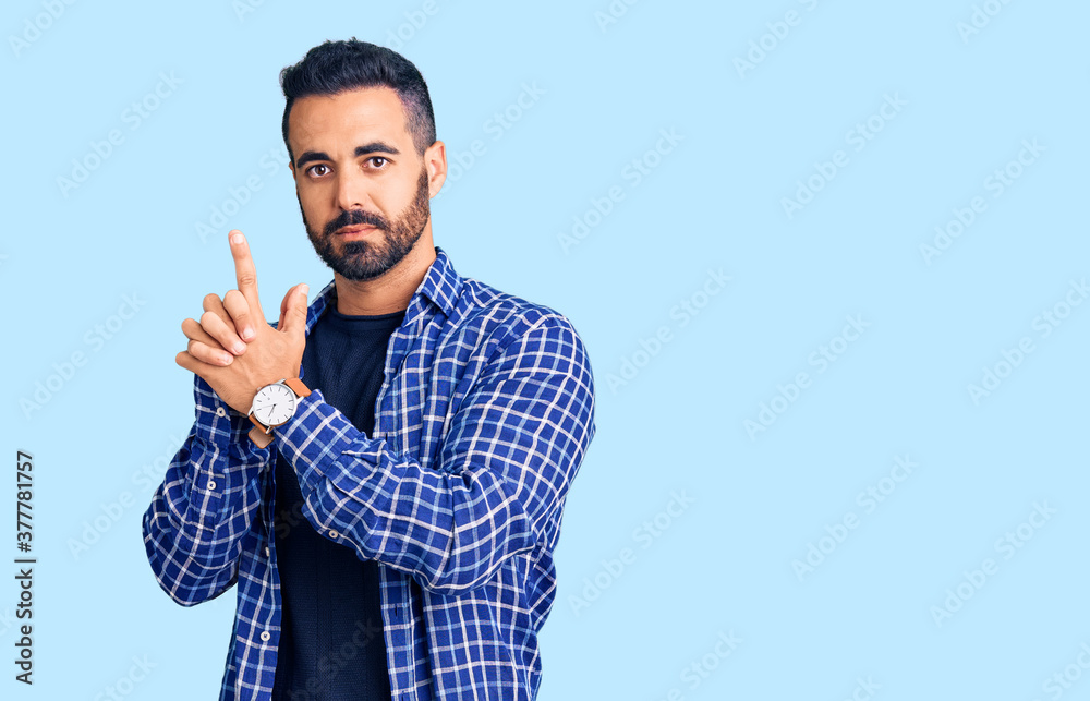 Young hispanic man wearing casual clothes holding symbolic gun with hand gesture, playing killing shooting weapons, angry face Young hispanic man wearing casual clothes holding symbolic gun with hand gesture, playing killing shooting weapons, angry face