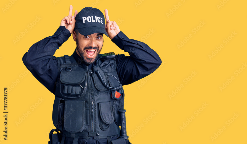 Young hispanic man wearing police uniform posing funny and crazy with fingers on head as bunny ears, smiling cheerful