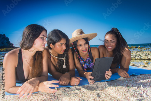 Four latin american ethnic girls friends using social media in digital tablet lying on sand Caribbean beach © GARSPHOTO