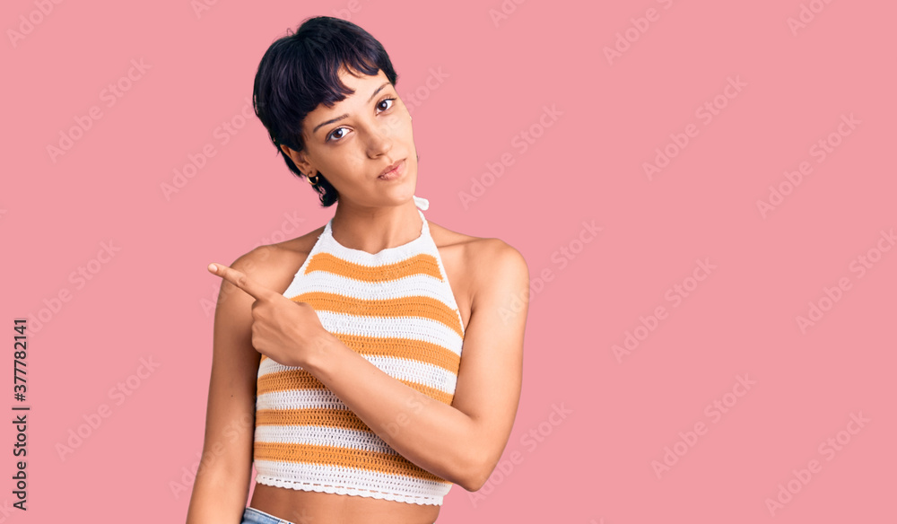 Young brunette woman with short hair wearing casual clothes pointing with hand finger to the side showing advertisement, serious and calm face Young brunette woman with short hair wearing casual clothes pointing with hand finger to the side showing advertisement, serious and calm face