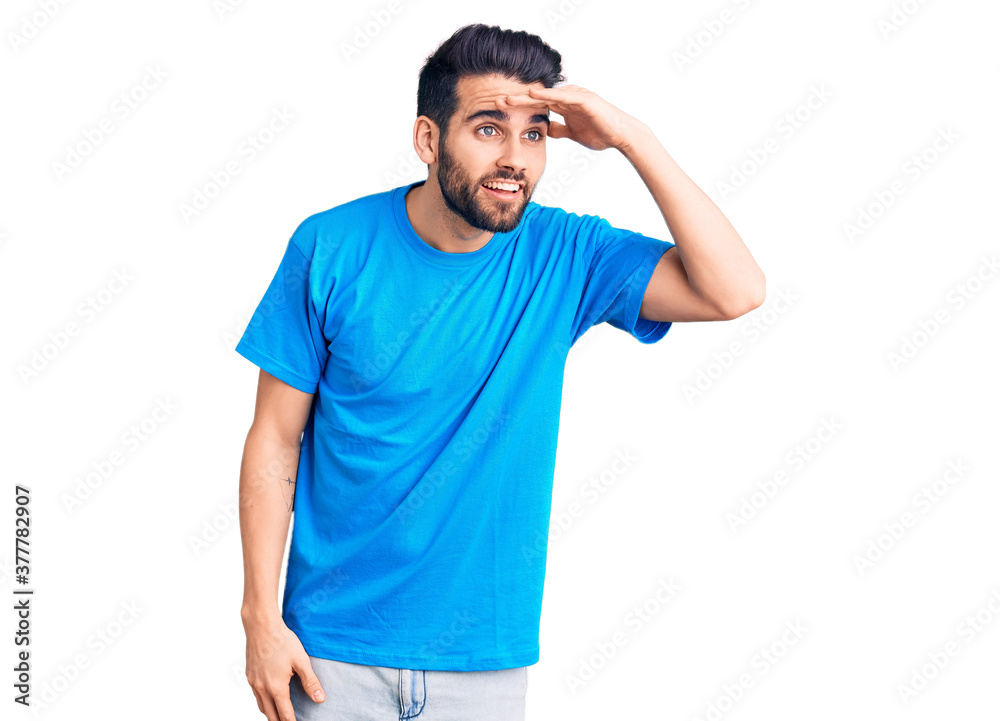 Young handsome man with beard wearing casual t-shirt very happy and smiling looking far away with hand over head. searching concept. Young handsome man with beard wearing casual t-shirt very happy and smiling looking far away with hand over head. searching concept.