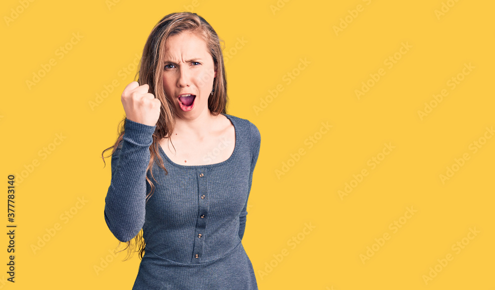 Young beautiful blonde woman wearing casual dress angry and mad raising fist frustrated and furious while shouting with anger. rage and aggressive concept. Young beautiful blonde woman wearing casual dress angry and mad raising fist frustrated and furious while shouting with anger. rage and aggressive concept.
