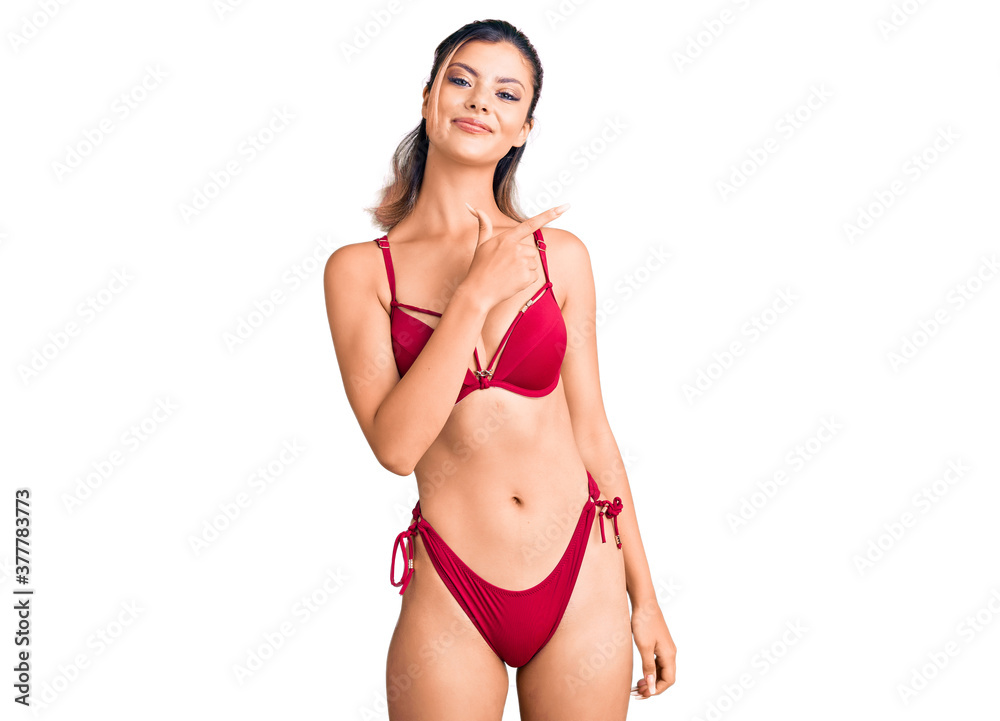 Naklejka premium Young beautiful woman wearing bikini cheerful with a smile on face pointing with hand and finger up to the side with happy and natural expression