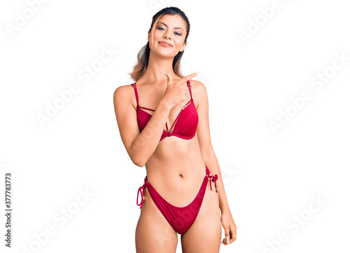 Young beautiful woman wearing bikini cheerful with a smile on face pointing with hand and finger up to the side with happy and natural expression © Krakenimages.com