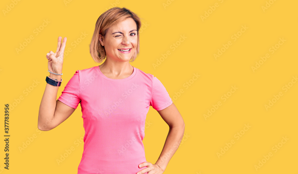 Young blonde woman wearing sportswear smiling with happy face winking at the camera doing victory sign with fingers. number two. Young blonde woman wearing sportswear smiling with happy face winking at the camera doing victory sign with fingers. number two.