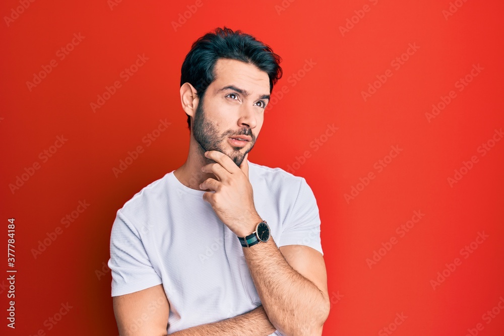 Young hispanic man wearing casual white tshirt thinking worried about a question, concerned and nervous with hand on chin Young hispanic man wearing casual white tshirt thinking worried about a question, concerned and nervous with hand on chin