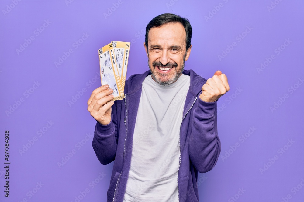 Middle age handsome tourist man holding airline boarding pass over isolated purple background screaming proud, celebrating victory and success very excited with raised arm Middle age handsome tourist man holding airline boarding pass over isolated purple background screaming proud, celebrating victory and success very excited with raised arm