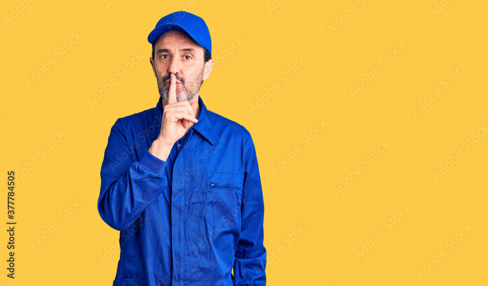 Middle age handsome man wearing mechanic uniform asking to be quiet with finger on lips. silence and secret concept.