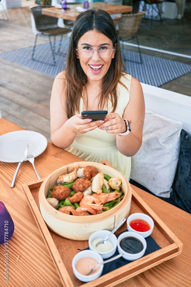 Young beautiful hispanic woman smiling happy. Sitting on the table using smartphone to make food picture at restaurant Young beautiful hispanic woman smiling happy. Sitting on the table using smartphone to make food picture at restaurant