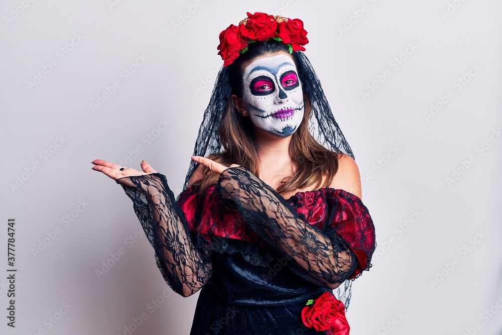 Young woman wearing day of the dead costume over white amazed and smiling to the camera while presenting with hand and pointing with finger.