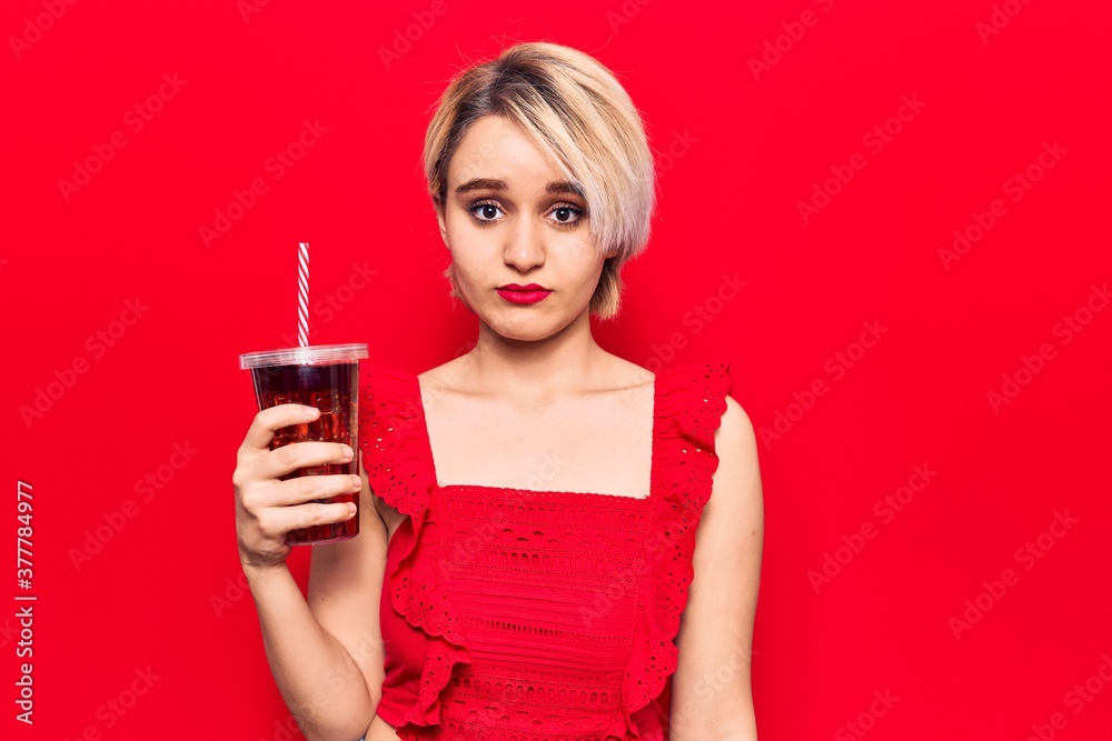 Young beautiful blonde woman drinking glass of cola beverage thinking attitude and sober expression looking self confident Young beautiful blonde woman drinking glass of cola beverage thinking attitude and sober expression looking self confident