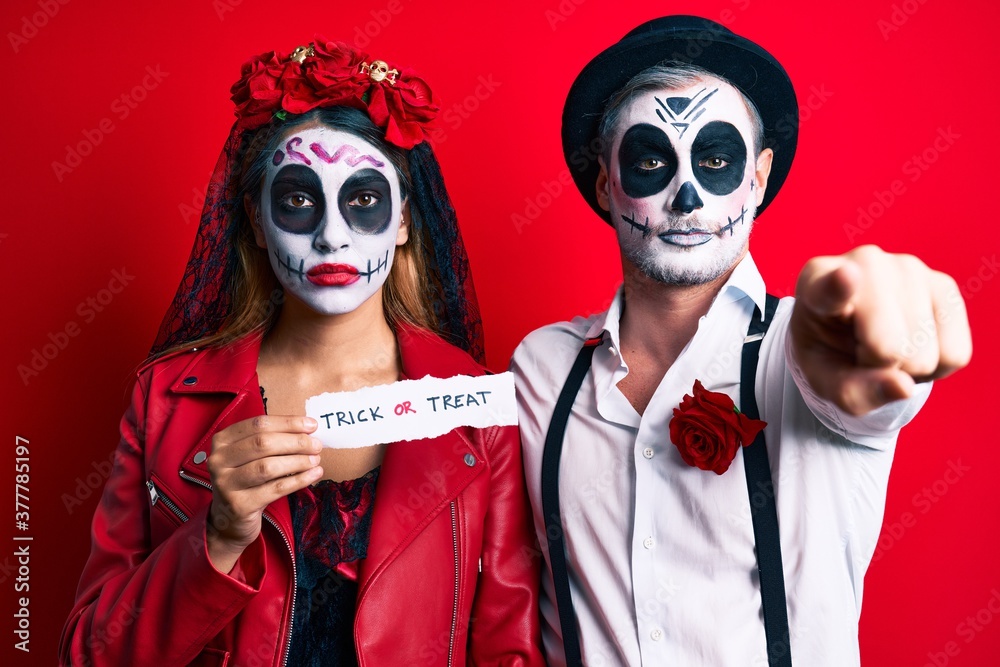 Couple wearing day of the dead costume holding trick or treat paper pointing with finger to the camera and to you, confident gesture looking serious Couple wearing day of the dead costume holding trick or treat paper pointing with finger to the camera and to you, confident gesture looking serious