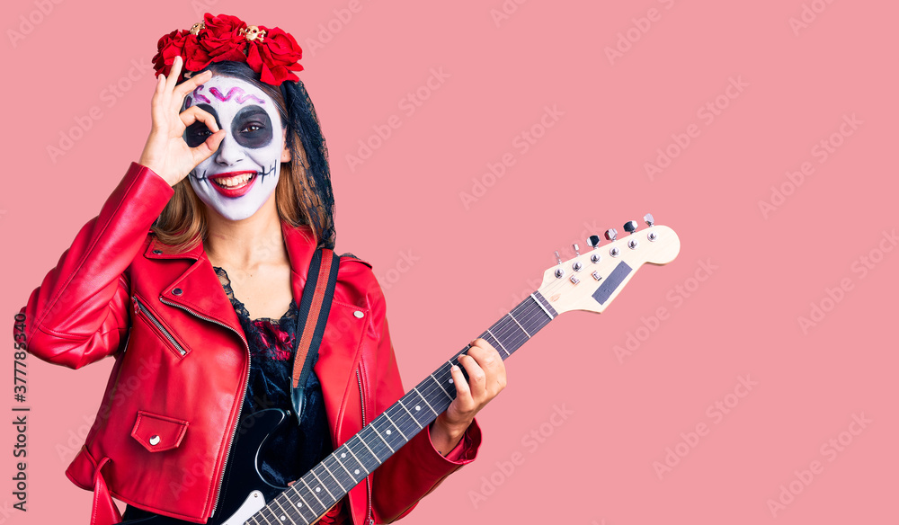Woman wearing day of the dead costume playing electric guitar smiling happy doing ok sign with hand on eye looking through fingers Woman wearing day of the dead costume playing electric guitar smiling happy doing ok sign with hand on eye looking through fingers